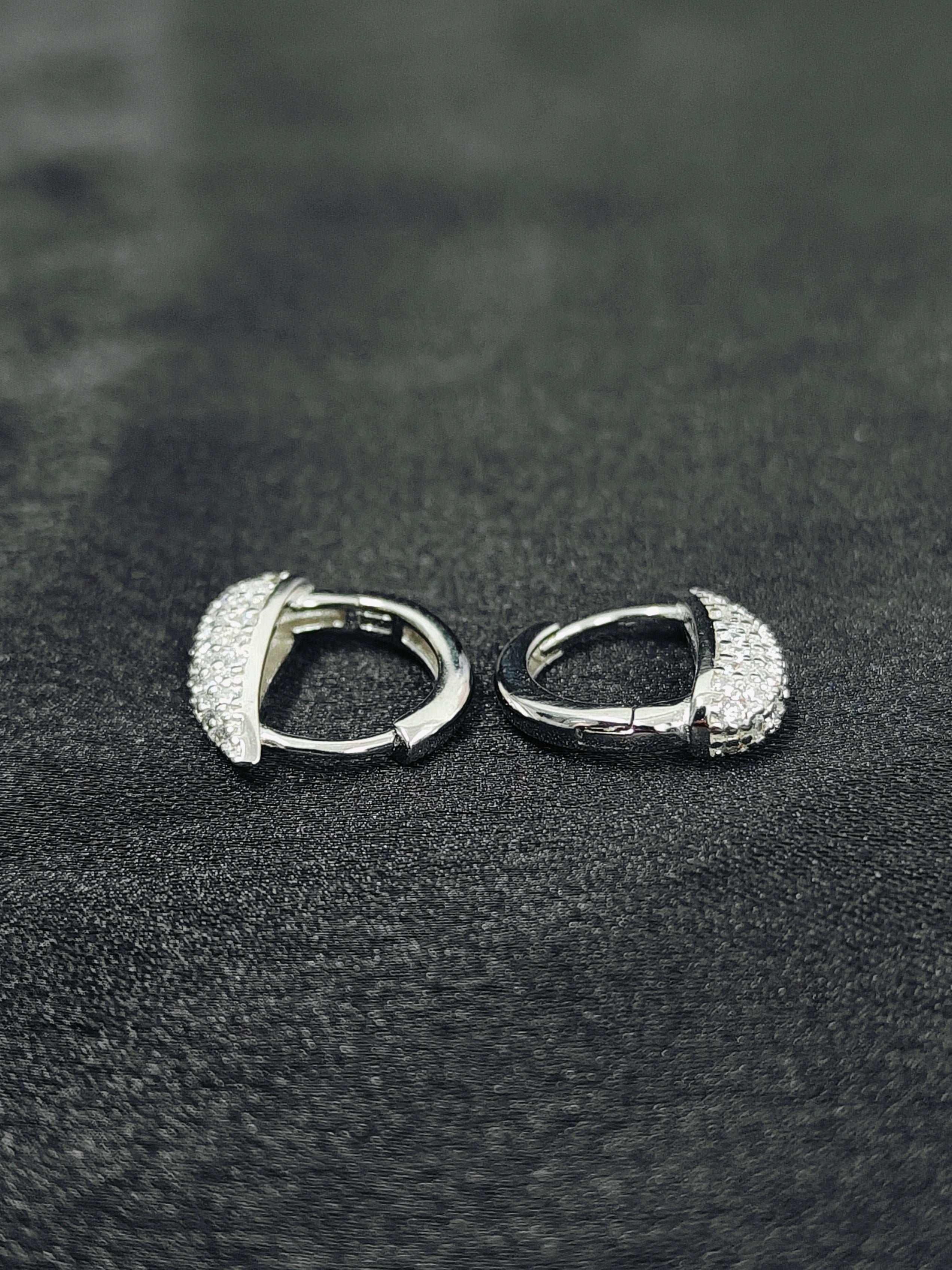 Pair of silver hoop earrings on a black textured surface